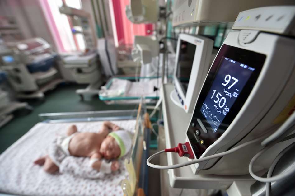a newborn in bed plugged to a machine reading it's vitals