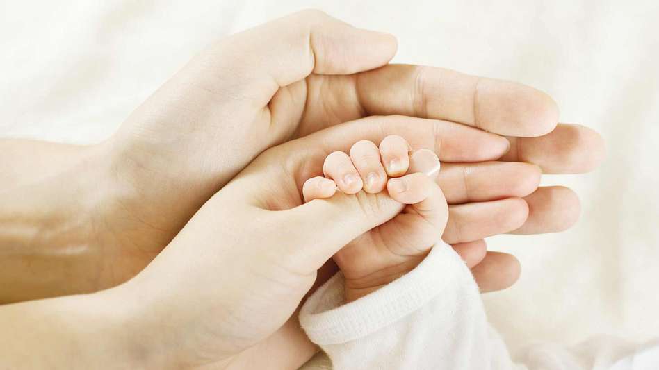 Parents holding hands with their new born baby