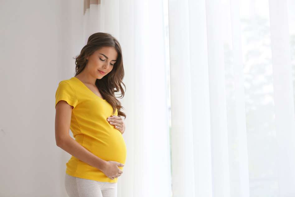 Pregnant woman standing, cradling her baby wearing a yellow top