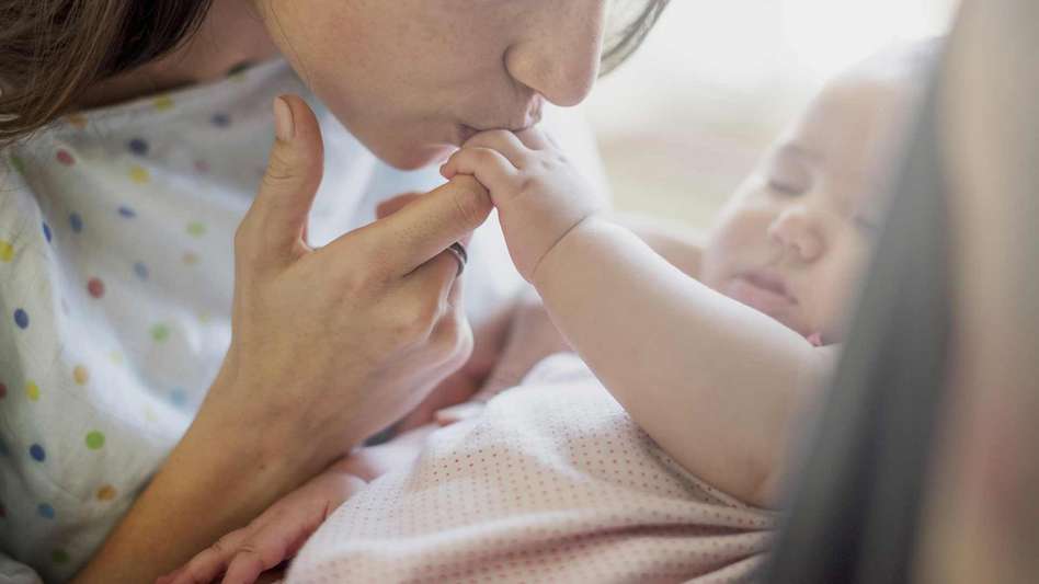 Postnatal depression article - New mother kissing her newborns hand