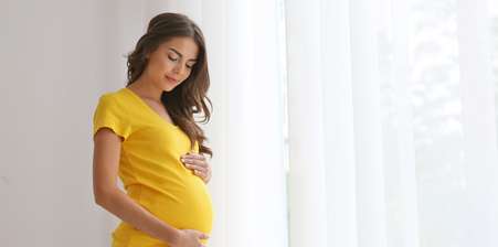 Pregnant woman standing, cradling her baby wearing a yellow top
