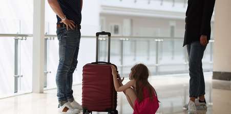 Separated couple talking over holiday childcare with child crouching by the suitcase
