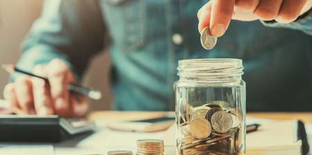 Person adding coins in a glass jar as savings
