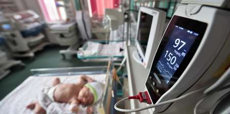 a newborn in bed plugged to a machine reading it's vitals