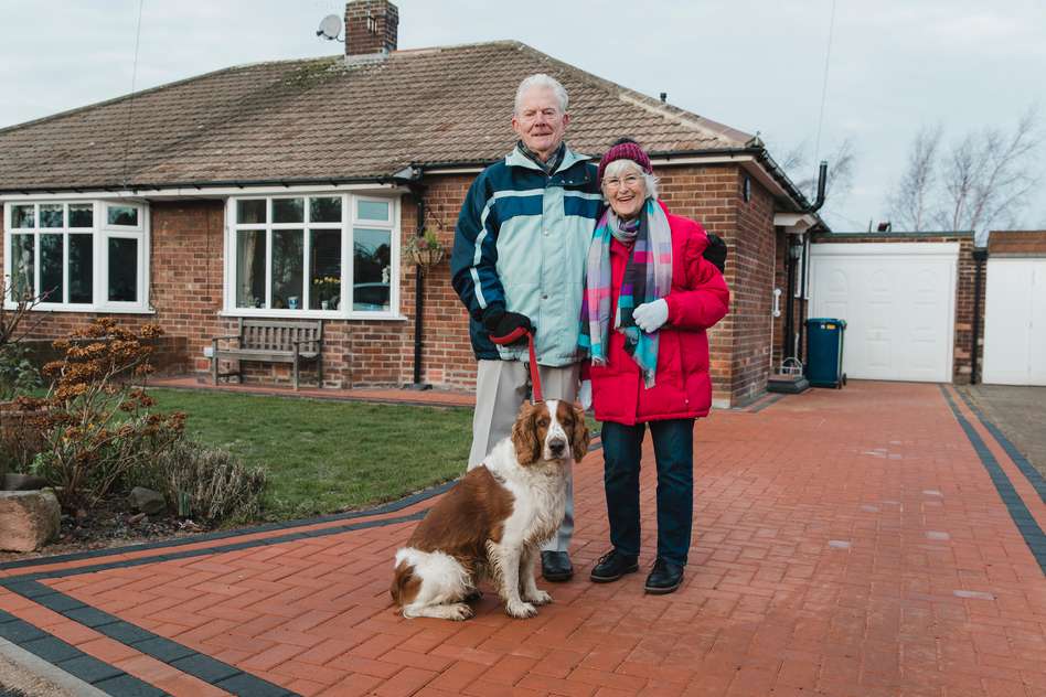 Elderly English couple outside their house with their dog