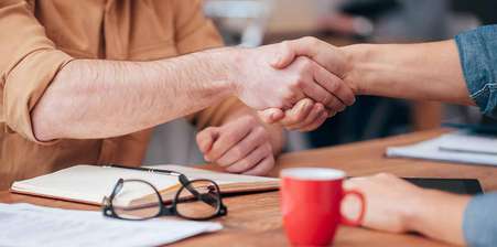 Two business people shaking hands over a coffee