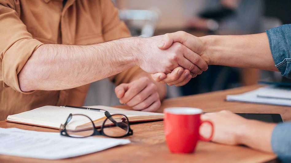 Two business people shaking hands over a coffee